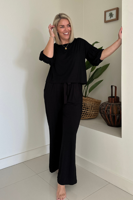 Front full-body view of woman in the Lexi Bamboo Top with Alexa Pants in black, arms open and smiling.