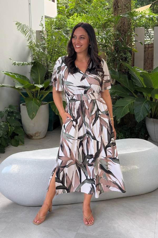Woman wearing the Kylie Bamboo Dress in Tropical Palm, front view showing the wrap neckline and smocked waist with hand in pocket